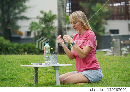 Young woman beading colorful bracelets outdoors in a park Young woman beading colorful bracelets outdoors in a park 130587692