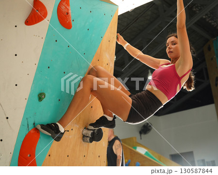 A strong female climber climbs an artificial wall with colorful grips A strong female climber climbs an artificial wall with colorful grips 130587844