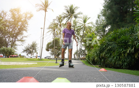 A woman is rollerblading gracefully on a road located in a park 130587881