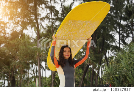 Young woman wearing tight wetsuit is going to surfboard at beautiful beach 130587937