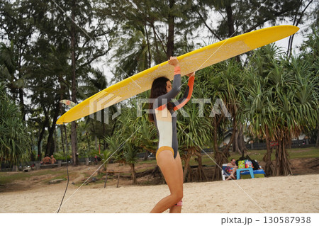 Young woman wearing tight wetsuit is going to surfboard at beautiful beach Young woman wearing tight wetsuit is going to surfboard at beautiful beach 130587938