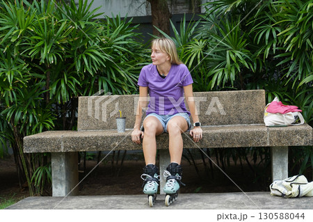 A woman is sitting on a bench and putting on her roller skates 130588044