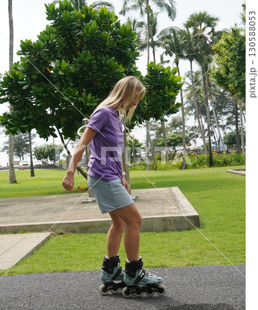A woman is rollerblading gracefully on a road located in a park A woman is rollerblading gracefully on a road located in a park 130588053