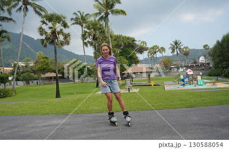 A woman is rollerblading gracefully on a road located in a park 130588054