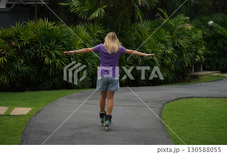 A woman is rollerblading gracefully on a road located in a park 130588055