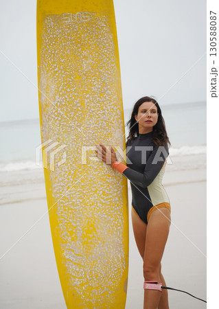 A woman in a stylish wet suit confidently holds a surfboard on the beach A woman in a stylish wet suit confidently holds a surfboard on the beach 130588087