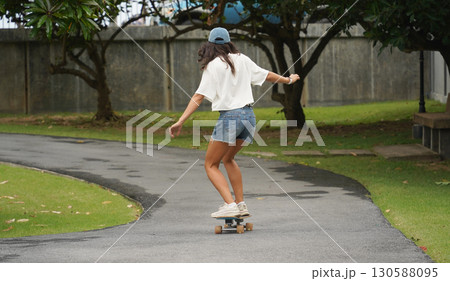A young woman is skillfully riding a skateboard down a scenic park 130588095