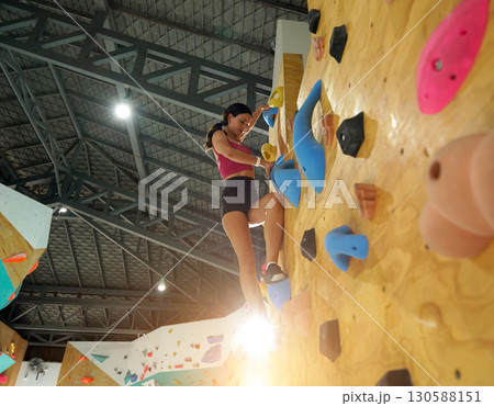 A strong female climber climbs an artificial wall with colorful grips 130588151