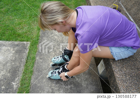 A woman is sitting on a bench and putting on her roller skates 130588177
