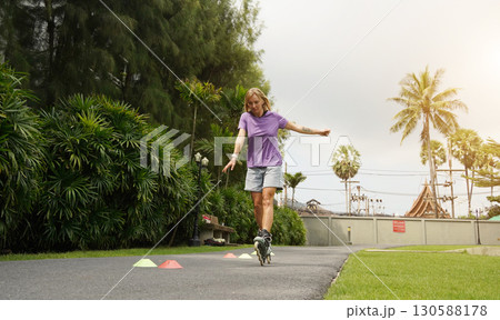 A woman is rollerblading gracefully on a road located in a park 130588178