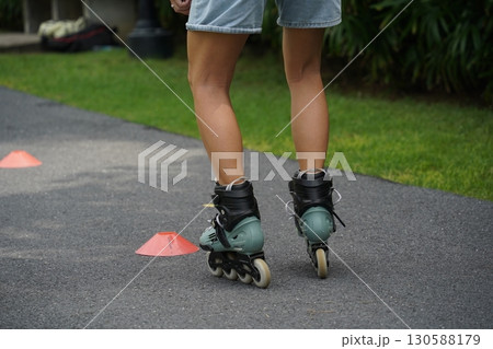 A woman is rollerblading gracefully on a road located in a park 130588179