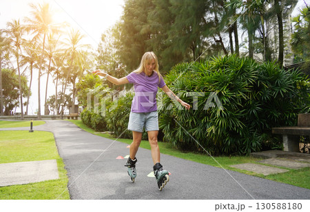 A woman is rollerblading gracefully on a road located in a park 130588180