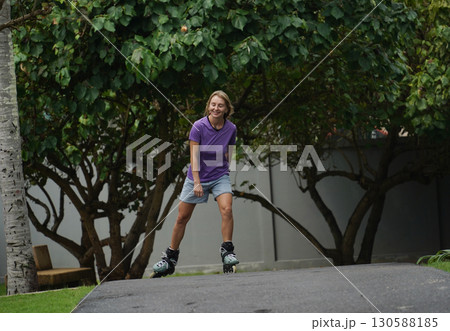 A woman is rollerblading gracefully on a road located in a park 130588185