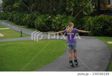 A woman is rollerblading gracefully on a road located in a park 130588189