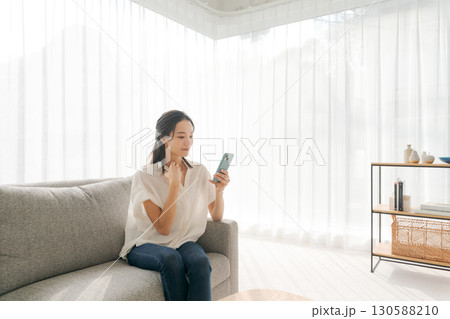 リビングのソファーでスマホを操作する女性 130588210