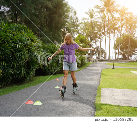 A woman is rollerblading gracefully on a road located in a park 130588299