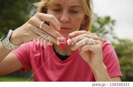 Young woman beading colorful bracelets outdoors in a park 130588322