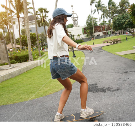 A young woman is skillfully riding a skateboard down a scenic park 130588466