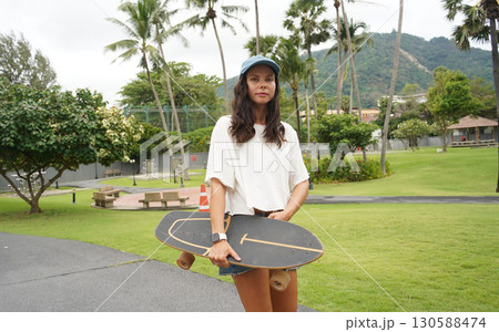 A woman is walking at the city park while carrying a skateboard in her hands 130588474