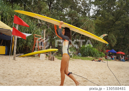 Young woman wearing tight wetsuit is going to surfboard at beautiful beach Young woman wearing tight wetsuit is going to surfboard at beautiful beach 130588481