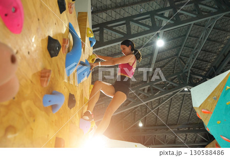 A strong female climber climbs an artificial wall with colorful grips A strong female climber climbs an artificial wall with colorful grips 130588486