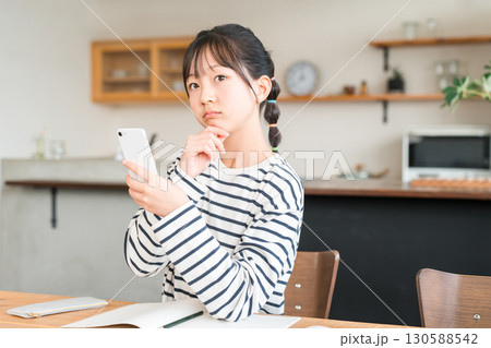 自宅のリビング・ダイニングでスマホを使う小学生・中学生の女の子 自宅のリビング・ダイニングでスマホを使う小学生・中学生の女の子 130588542