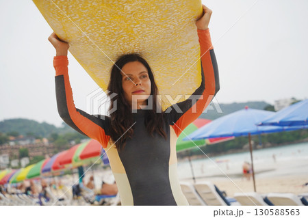 Young woman wearing tight wetsuit is going to surfboard at beautiful beach Young woman wearing tight wetsuit is going to surfboard at beautiful beach 130588563