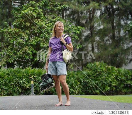 A woman is rollerblading gracefully on a road located in a park A woman is rollerblading gracefully on a road located in a park 130588628