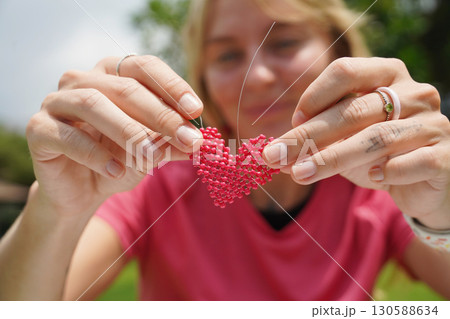 Young woman beading colorful bracelets outdoors in a park Young woman beading colorful bracelets outdoors in a park 130588634
