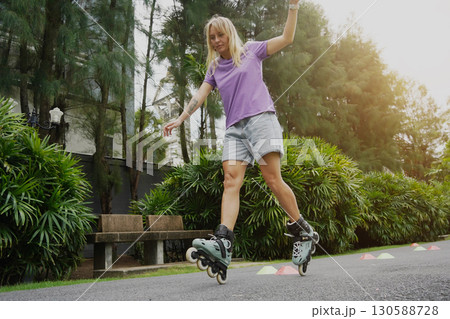 A woman is rollerblading gracefully on a road located in a park 130588728