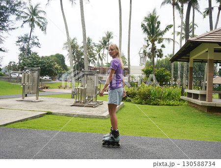 A woman is rollerblading gracefully on a road located in a park A woman is rollerblading gracefully on a road located in a park 130588734