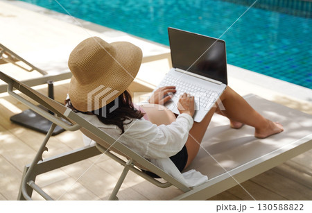 A pregnant woman is comfortably seated on a lounge chair using her laptop A pregnant woman is comfortably seated on a lounge chair using her laptop 130588822