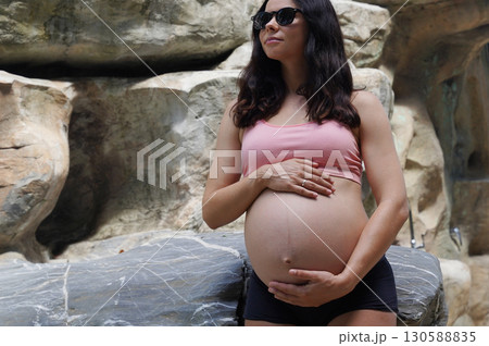 A pregnant woman is gracefully standing in front of a beautiful waterfall rock 130588835