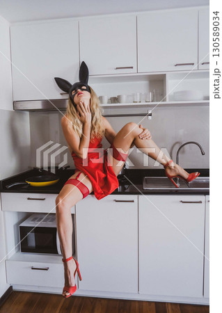 A woman in a striking black bunny mask is perched on a kitchen counter A woman in a striking black bunny mask is perched on a kitchen counter 130589034