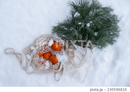 Ripe tangerines in reusable mesh bag with fir branch and garland outside in snowy winter. Concept of sustainable Christmas celebration, responsibility and inclusivity. Oranges Ripe tangerines in reusable mesh bag with fir branch and garland outside in snowy winter. Concept of sustainable Christmas celebration, responsibility and inclusivity. Oranges 130590810