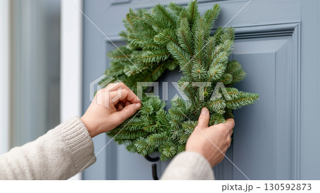 Person decorating front door with festive green wreath for holiday season 130592873