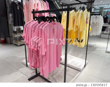 Pink and yellow t-shirts are organized on racks in a fashion retail environment. Shopping, consumer lifestyle, seasonal color trend and commerce in contemporary textile industry. 130595617