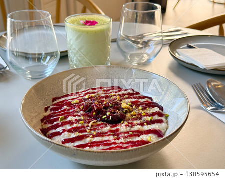 Bowl of creamy oat pudding with raspberry sauce and crushed pistachios served on table. Dessert, sweet food, and culinary creativity in modern dining concept. 130595654