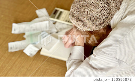 電卓とレシートの前で悩む高齢女性_左向きななめ 電卓とレシートの前で悩む高齢女性_左向きななめ 130595878