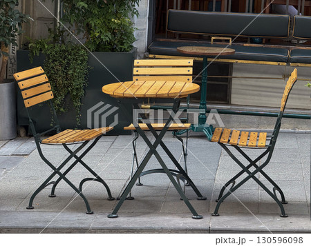 Outdoor cafe chairs and table with wooden slats. Urban lifestyle, relaxation, and leisure. Outdoor cafe chairs and table with wooden slats. Urban lifestyle, relaxation, and leisure. 130596098