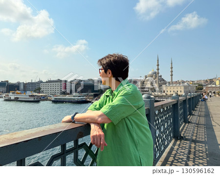 Woman in green dress looking at the Bosphorus from Galata Bridge. Contemplation, travel, and urban lifestyle by the sea. 130596162