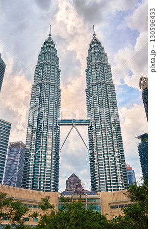 Nov 20, 2019 - Kuala Lumpur, Malaysia: Petronas Twin Towers with skybridge in urban skyline at day under dramatic cloudy blue sky. Scenic cityscape with lush park, modern Suria KLCC shopping mall in Nov 20, 2019 - Kuala Lumpur, Malaysia: Petronas Twin Towers with skybridge in urban skyline at day under dramatic cloudy blue sky. Scenic cityscape with lush park, modern Suria KLCC shopping mall in 130596433