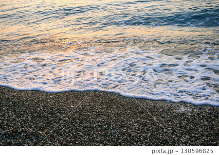Gentle sea waves lapping against a pebbled shore at sunset creating a serene coastal atmosphere 130596825