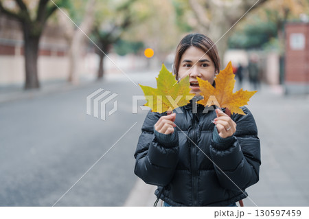 Female tourist holding yellow maple leaves and sightseeing on Anfu road in autumn. Woman traveler visiting Shanghai, China. Popular landmarks and tourist attractions in Shanghai. 130597459