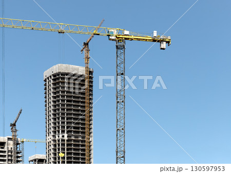 Construction site with tall unfinished highrise building, concrete structure, windows, scaffold, 130597953