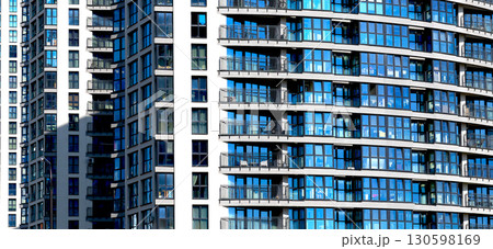 Modern apartment building close up with glass windows, geometric facade, sleek vertical structure. 130598169