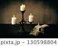Beautiful vintage cast iron candelabrum with three burning candles and goats skull on the table in the dark. 130598804