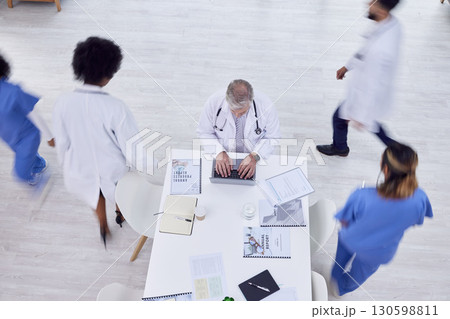 Doctor, man and laptop in busy hospital for medicine research, surgery schedule management or medical life insurance. Top view, healthcare worker and surgeon on technology with motion blur coworkers 130598811