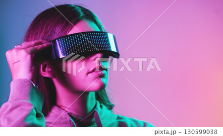 Virtual reality, cyberpunk and mockup, woman in goggles in online metaverse app, game or video on neon purple background. Vr, ar and ux, future fashion digital glasses on model in studio with space. Virtual reality, cyberpunk and mockup, woman in goggles in online metaverse app, game or video on neon purple background. Vr, ar and ux, future fashion digital glasses on model in studio with space. 130599038