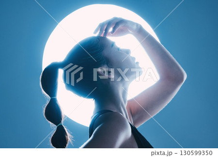 Beauty, light and profile of a model in a studio with a sensual, soft and attractive pose. Cosmetic, magical and slim woman with a mystical glow posing by a moon while isolated by a blue background. 130599350